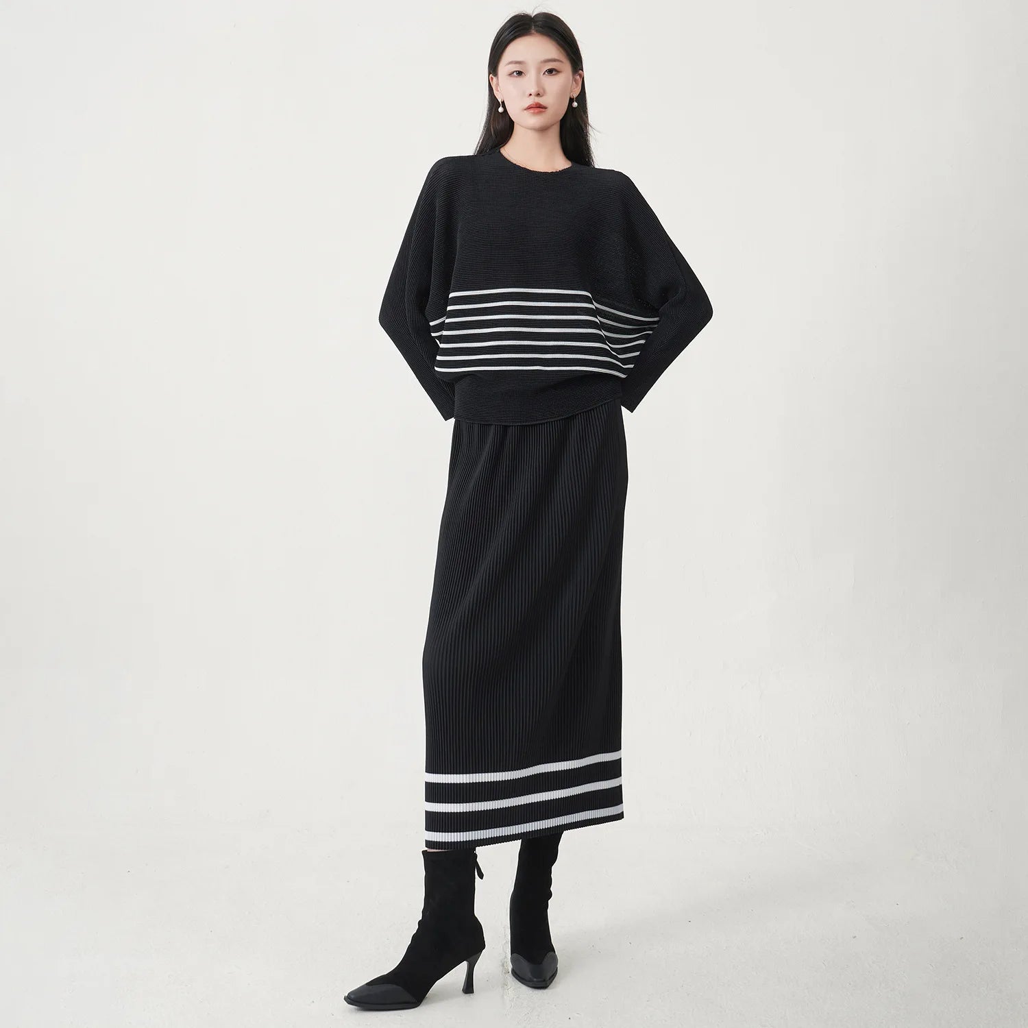 A trending women's clothing item for 2026: a matching black batwing-sleeved striped T-shirt and straight-cut skirt set by Miyake